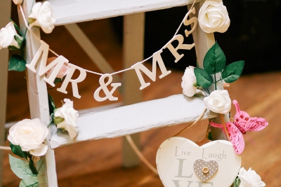 A white wooden ladder decorated with a "Mr & Mrs" banner, white roses, a heart ornament, and a pink butterfly.