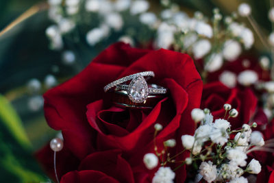 A pear-shaped engagement ring and wedding band resting on a red rose, surrounded by baby's breath flowers.