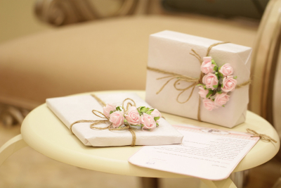 Two elegantly wrapped gift boxes with twine and pink rose embellishments, placed on a cream-colored table.