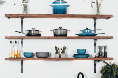 Wooden kitchen shelves displaying neatly arranged cookware, plates, glass bottles, and small potted plants.
