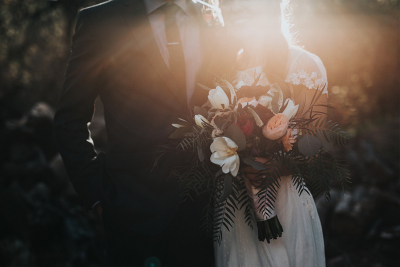 A couple embracing in soft golden sunlight, with the bride holding a bouquet of white and blush flowers.