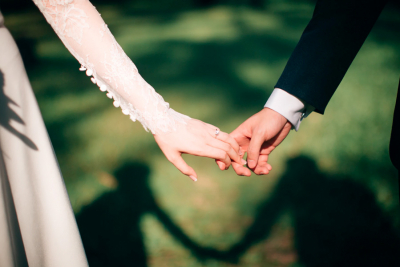 A bride and groom holding hands in soft sunlight, their shadows forming a heart shape on the grass.