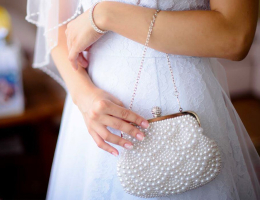 A bride in a white lace dress holding a pearl-covered clutch purse with a delicate chain, showcasing elegant wedding accessories.
