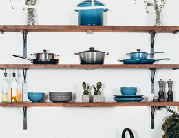 Wooden kitchen shelves displaying neatly arranged cookware, plates, glass bottles, and small potted plants.