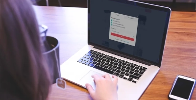 A person using a laptop with an open gift selection screen, with a phone and a tea mug on the wooden table.